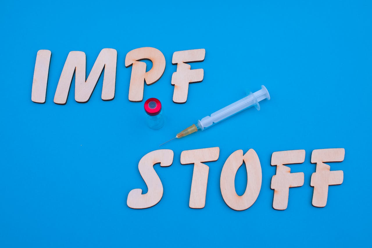 Wooden letters, syringe, and vial on blue background conveying vaccination theme.