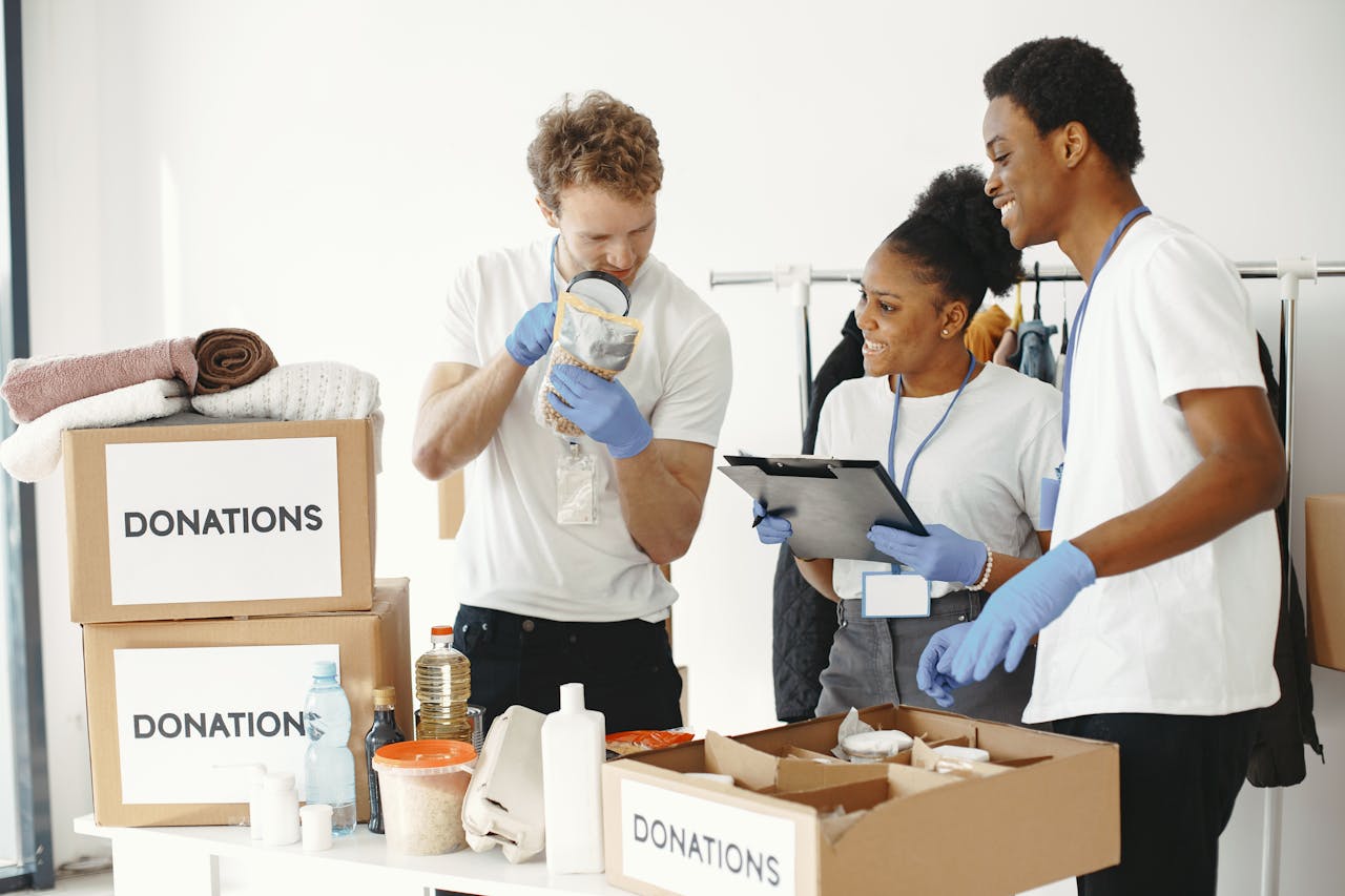 about-us Three diverse volunteers sorting donation boxes filled with clothing and supplies indoors.